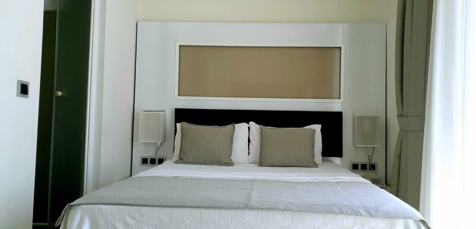 A hotel room with a large bed, a headboard with a screen, two bedside tables, and a curtain.