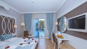 Une chambre d’hôtel avec un lit, un bureau avec des fruits, une chaise, une télévision et une vue sur la piscine.
