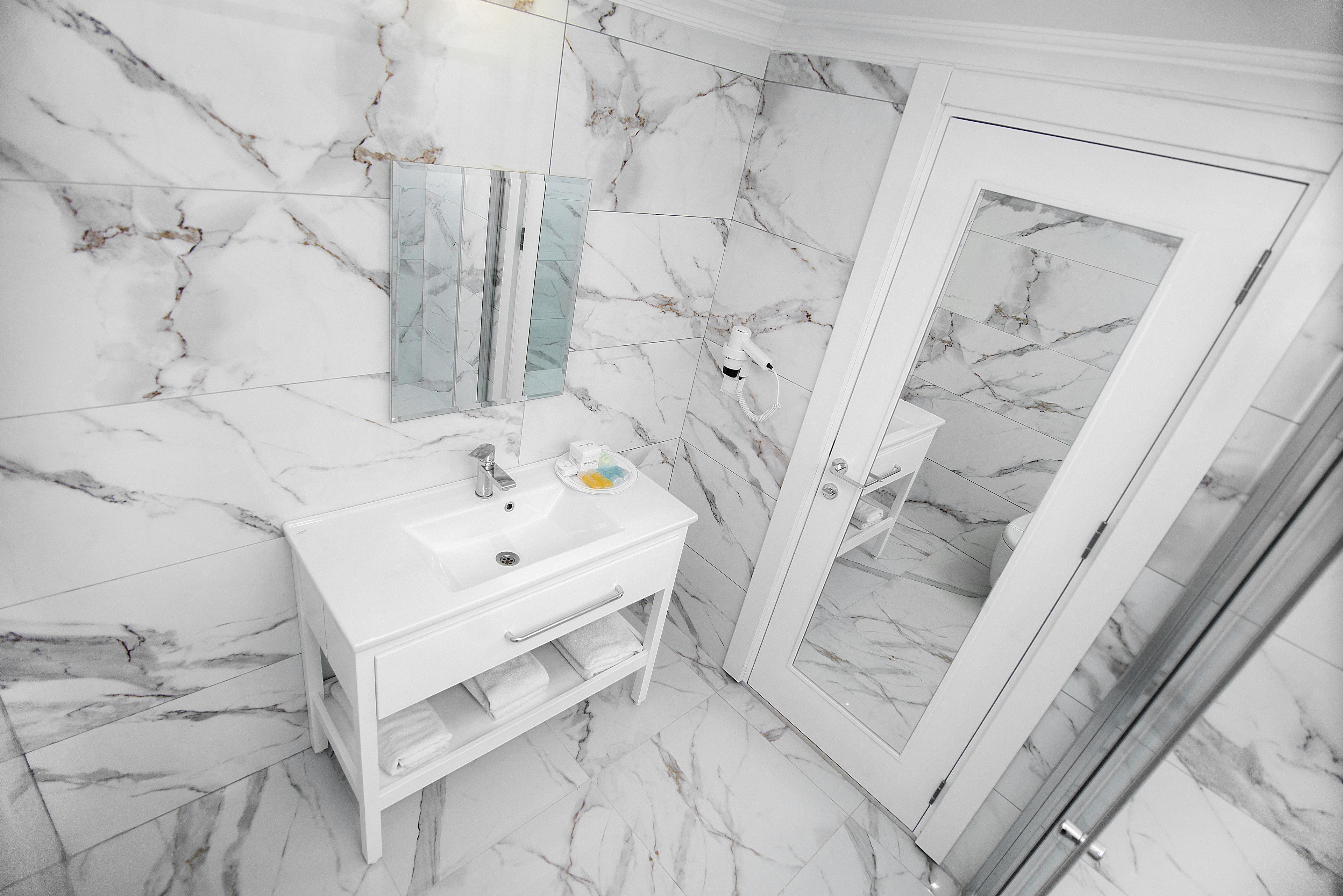 A bathroom with a white marble wall, a glass shower enclosure, and a white vanity with a mirror.