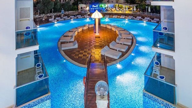Un espace piscine agrémenté d’un luminaire central, entouré de chaises longues et d’une terrasse en bois.