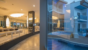 Un hall d’hôtel moderne doté d’un vaste espace salon, d’une piscine à laquelle on accède par une baie vitrée et d’un balcon à plusieurs niveaux.