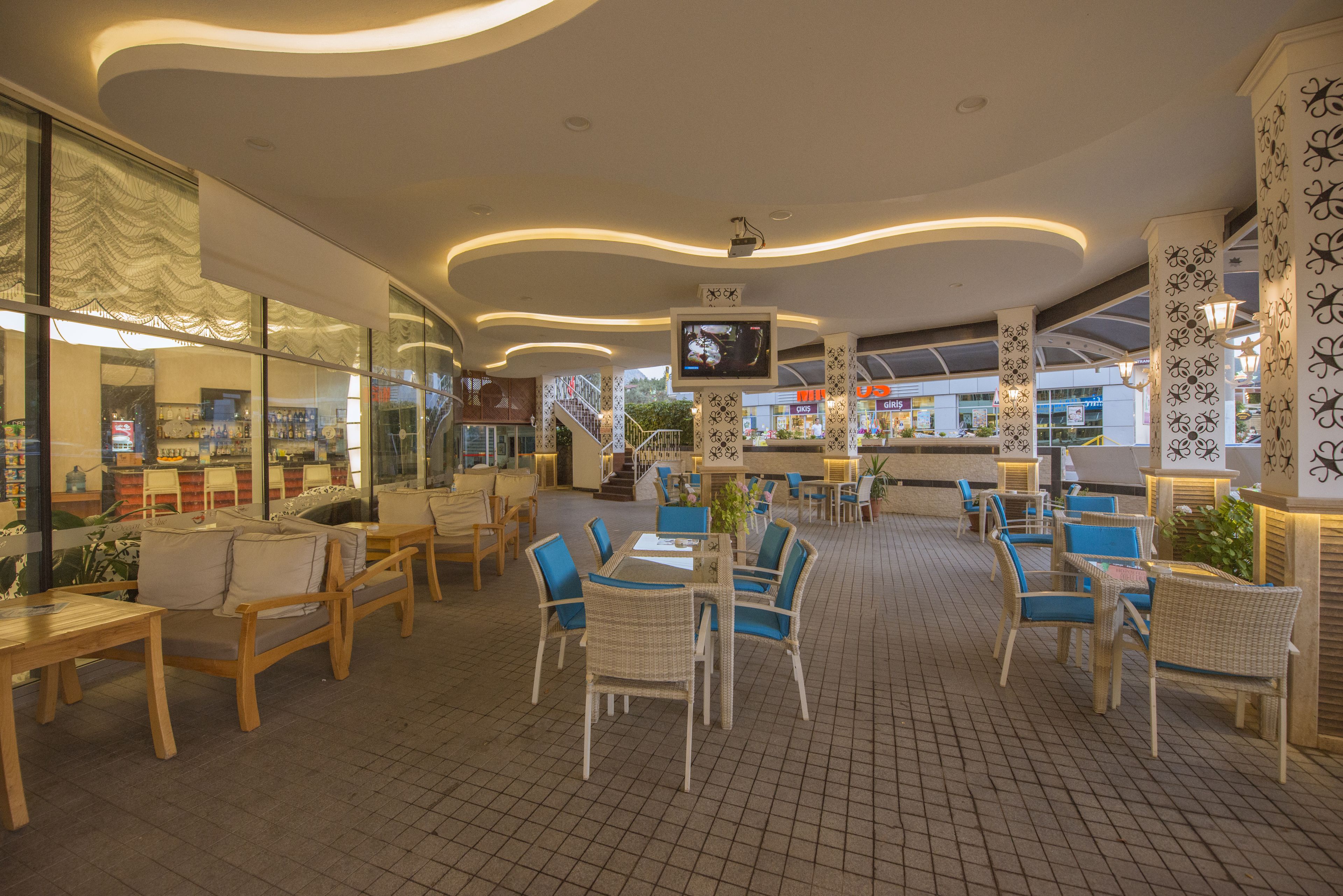 A spacious indoor area with wooden tables and chairs, a television mounted on the ceiling, and a patterned wall.