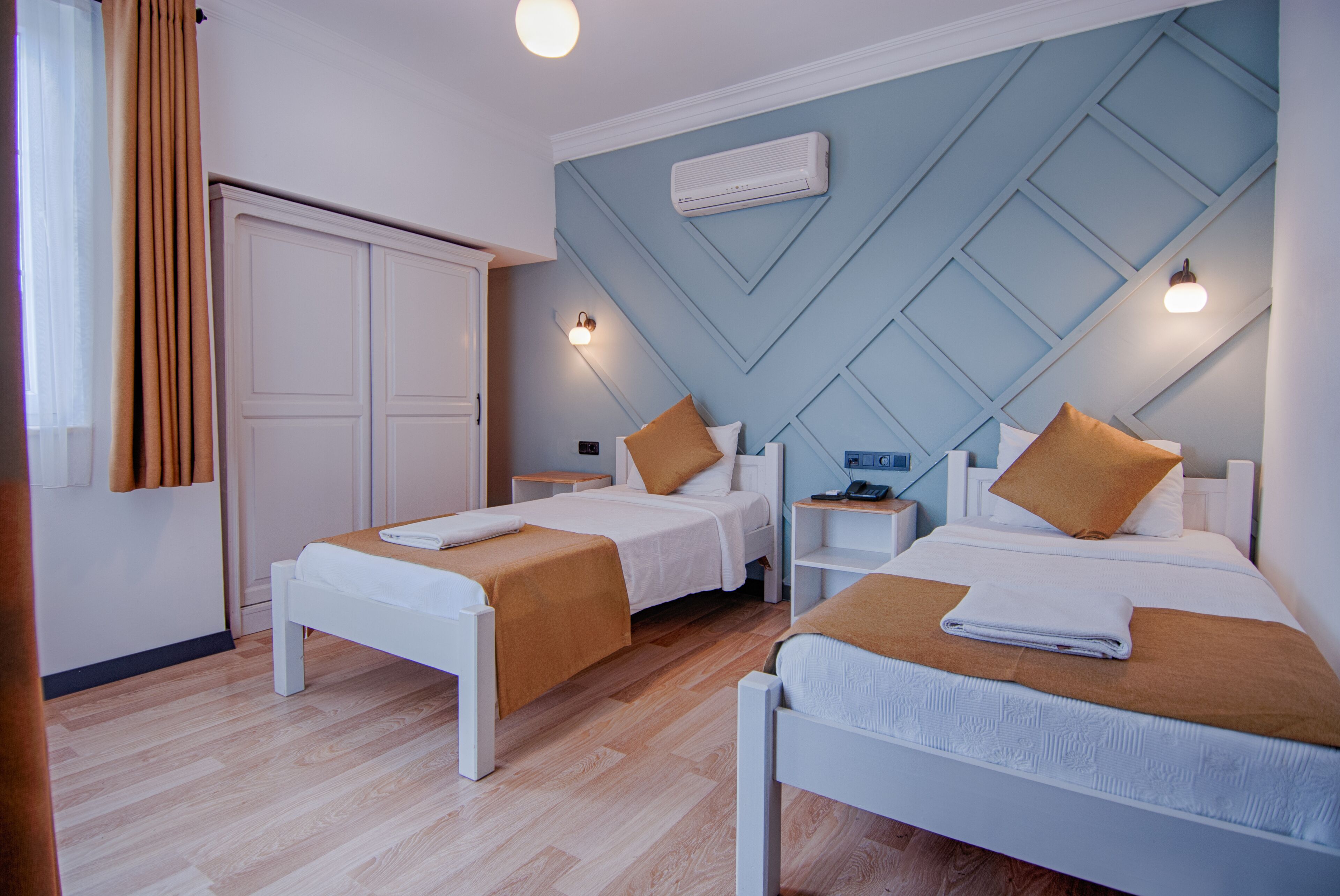 Habitación de hotel con dos camas individuales, un armario, una mesita de noche con lámpara y un equipo de aire acondicionado en la pared.
