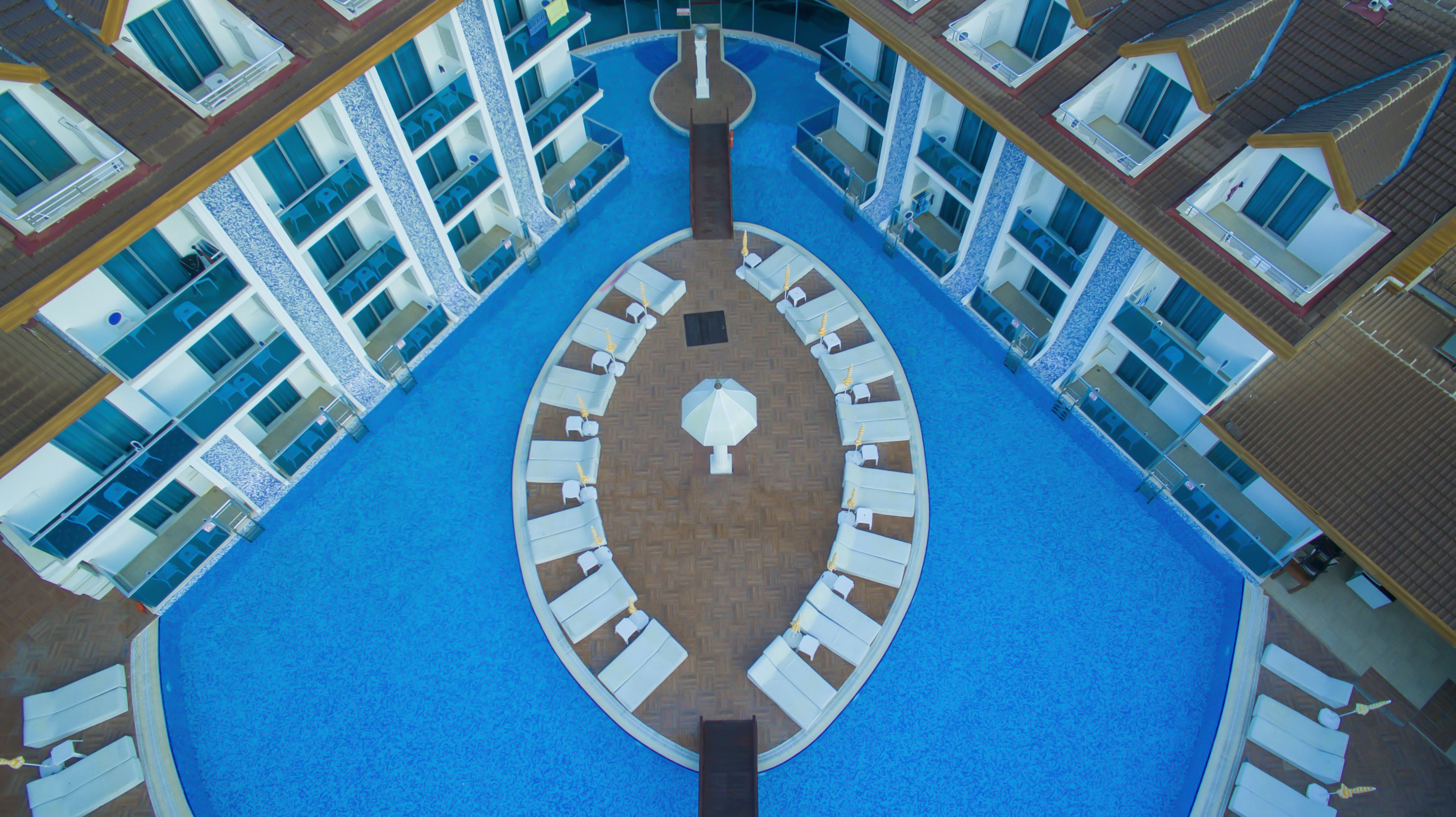 Un área de piscina circular con sillones de descanso y sombrillas, rodeada por varios balcones con ventanas.