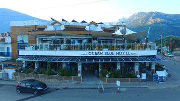 Hotel Ocean Blue, un edificio de dos pisos con zona de estar al aire libre y vistas a las montañas al fondo.