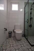 A bathroom with a toilet, a shower enclosure, patterned floor tiles, and a small window.
