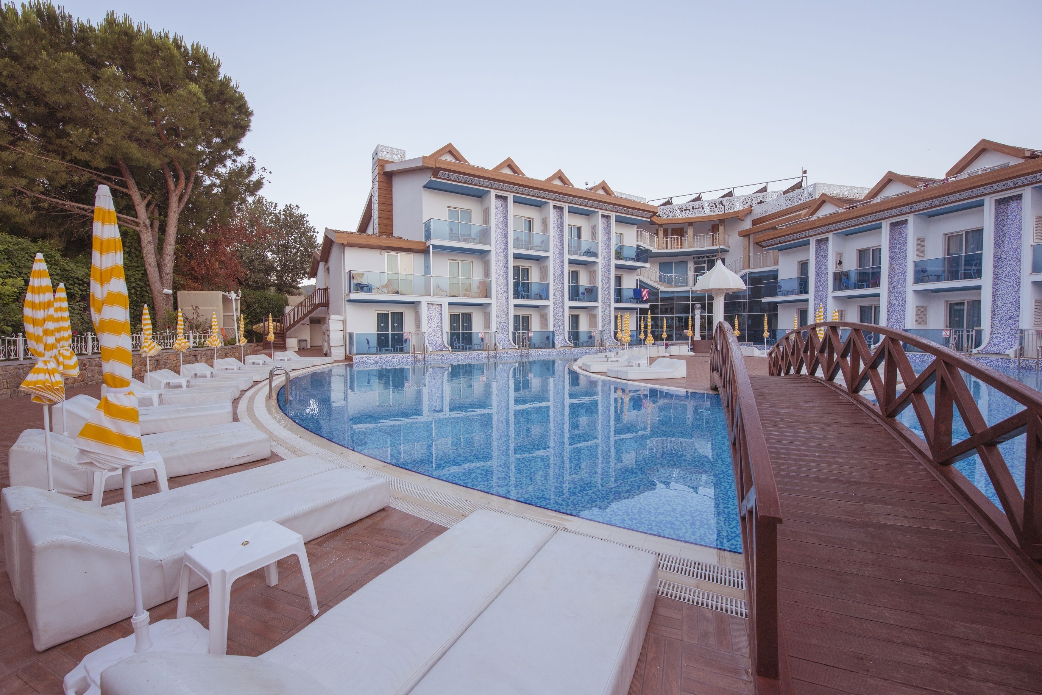 A swimming pool with lounge chairs and umbrellas, surrounded by a wooden deck and a building with multiple balconies.