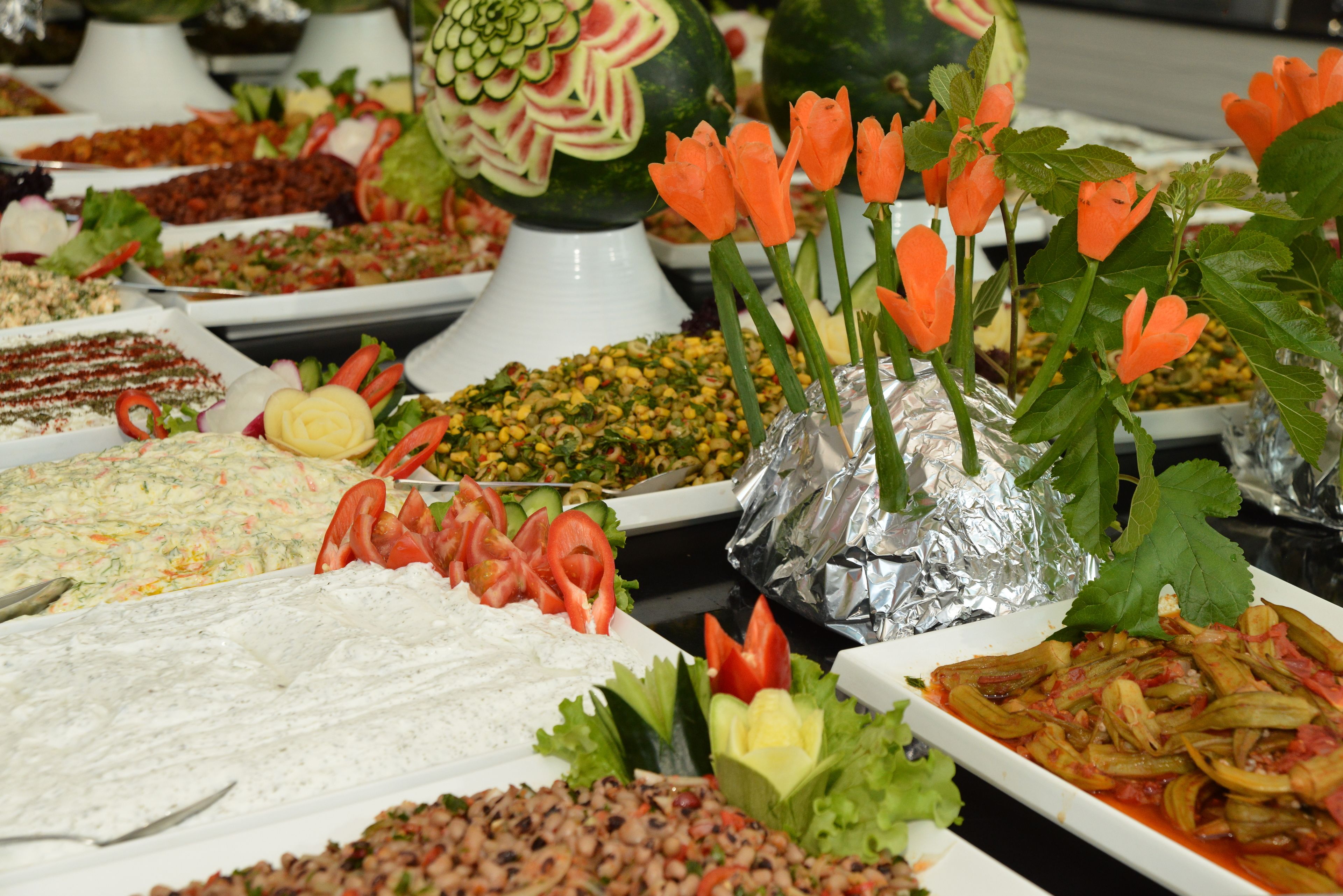 Ein Buffet mit verschiedenen Speisen, darunter Salate, Gemüse und einer Wassermelone als Mittelpunkt.