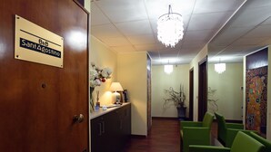 A reception area with a wooden door labeled "B&B SantAgostino," a reception desk, a chandelier, green chairs, and a hallway with a plant and artwork. - B&B Sant'Agostino (Milan)
