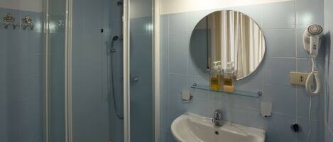 Een badkamer met een douche met glazen wand, een wit wastafelmeubel, een ronde spiegel en een haardroger aan de muur.