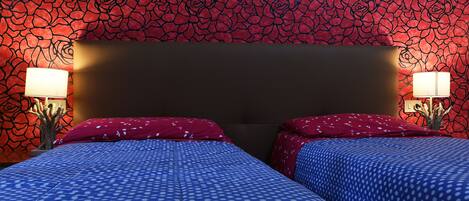 A room with two beds, red and blue polka dot bedspreads, and a red floral wallpaper.