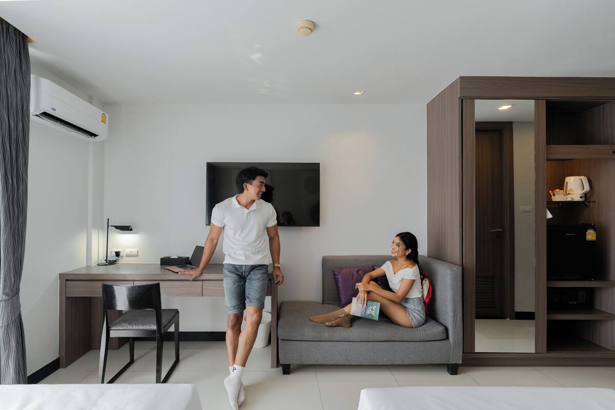 A modern hotel room with a desk, a sofa, a TV, and a wardrobe.