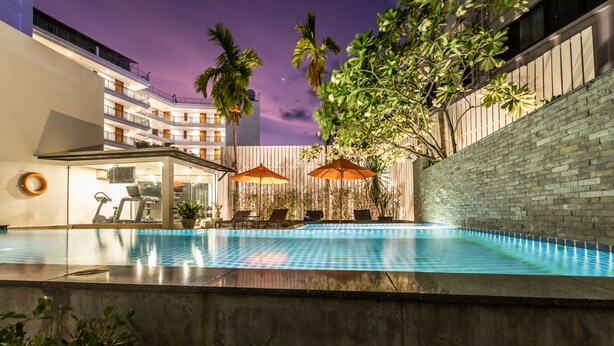 An outdoor swimming pool with lounge chairs and umbrellas, surrounded by a high-rise building with balconies and palm trees. - Citrus Patong Hotel by Compass Hospitality (Patong)