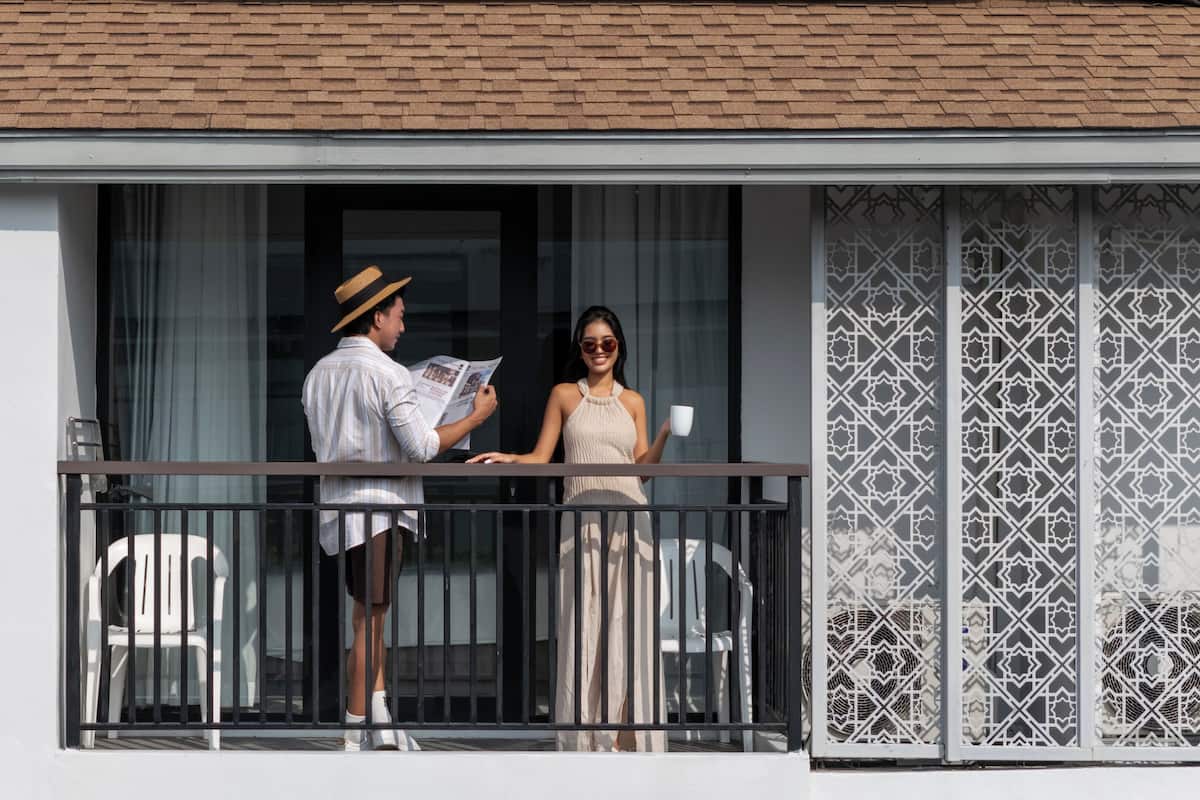 A balcony with a railing, a window with curtains, and a patterned wall.