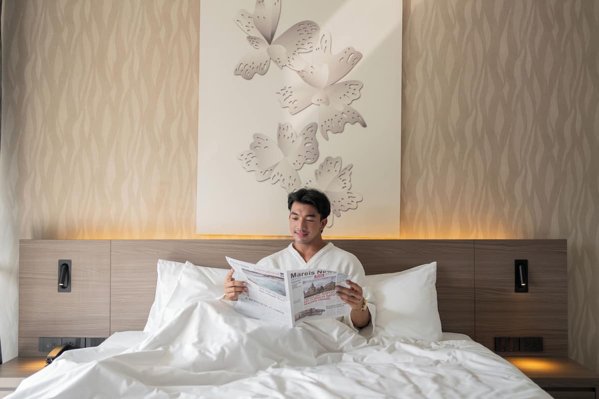 A person reading a book in a modern hotel room with a wooden headboard and a decorative wall panel.