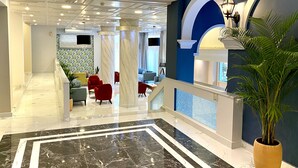 A spacious lobby with a marble floor, red and grey chairs, a staircase, and a large potted plant. - Hotel Paloma Blanca (Corfu)