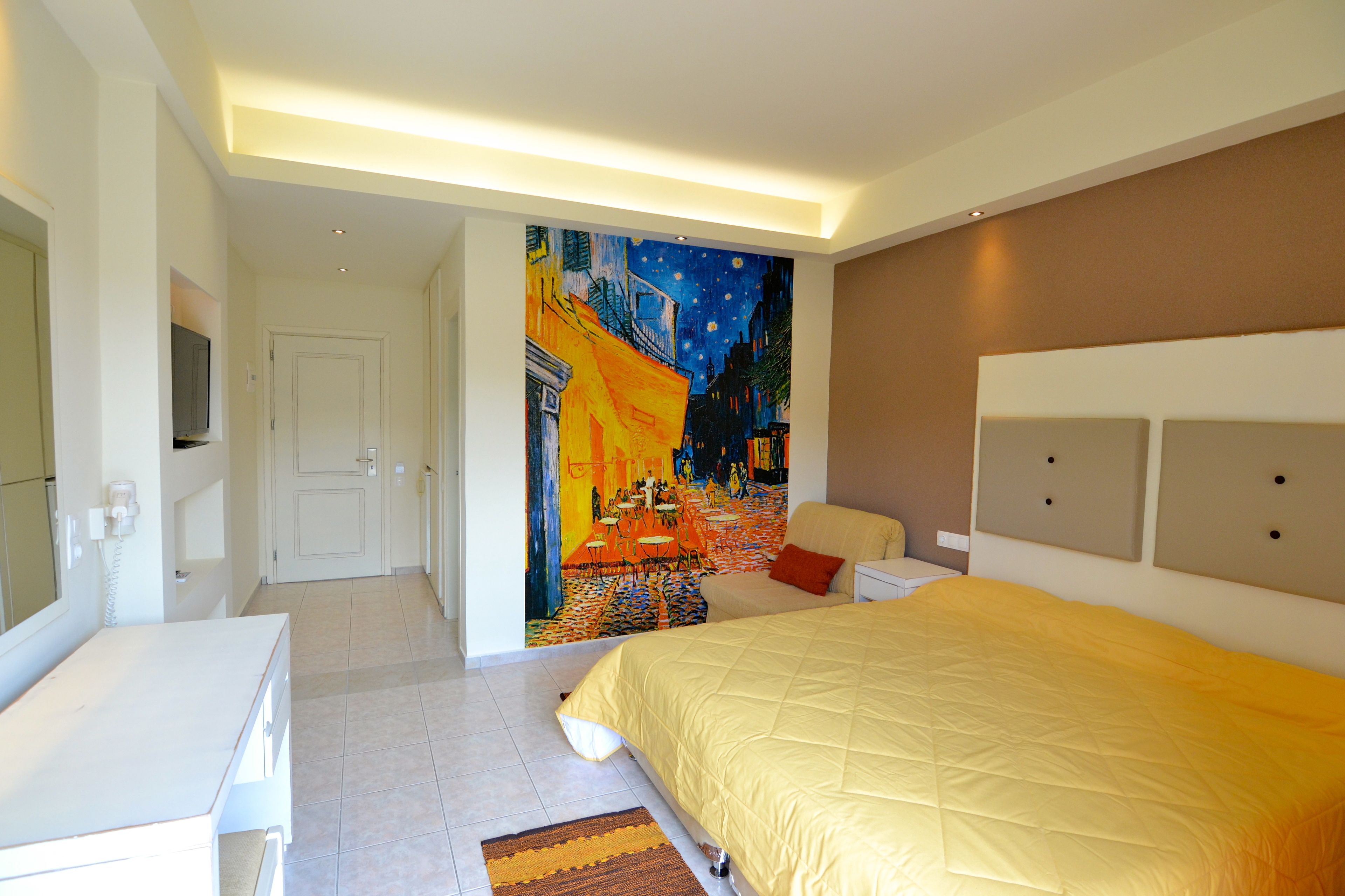 A bedroom with a large bed, a painting on the wall, and a white bedside table.