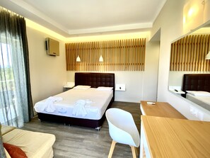 Habitación de hotel con cama, mesitas de noche, escritorio, silla, espejo y ventana con cortinas.