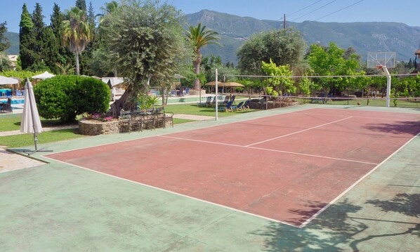 Una cancha de tenis con red, rodeada de vegetación y con una montaña al fondo.