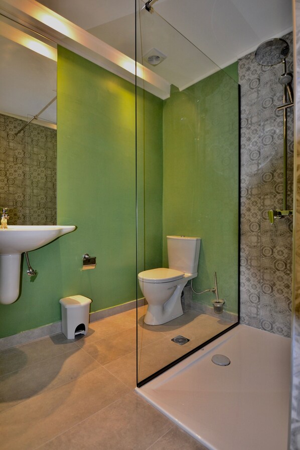 Un baño con pared verde, lavamanos blanco, inodoro y cabina de ducha con mampara de vidrio.