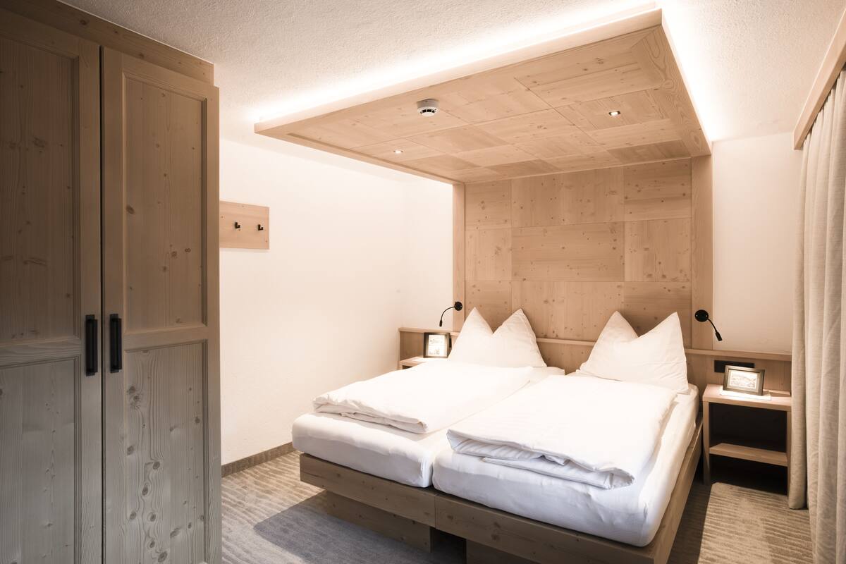 Ein Schlafzimmer mit einem hölzernen Kopfteil, einem Doppelbett, zwei Nachttischen mit Lampen und einem Kleiderschrank.
