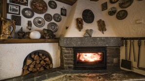 Een rustieke open haard met een stenen mantel, een houten plank met diverse decoratieve borden, en een verzameling aan de muur bevestigde objecten, waaronder een fox hoofd, een viool en meerdere ingelijste foto's.