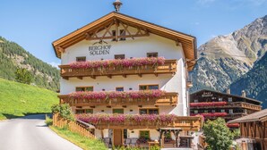 Een meerhoog gebouw met balkons versierd met bloemen, genaamd "BERGHOF SÖLDEN", op de achtergrond van een berglandschap.