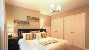 A bedroom with a bed, nightstands, a lamp, two doors, and wall art. - Boardwalk Homes - Executive Guest Rooms & Townhomes (Kitchener)