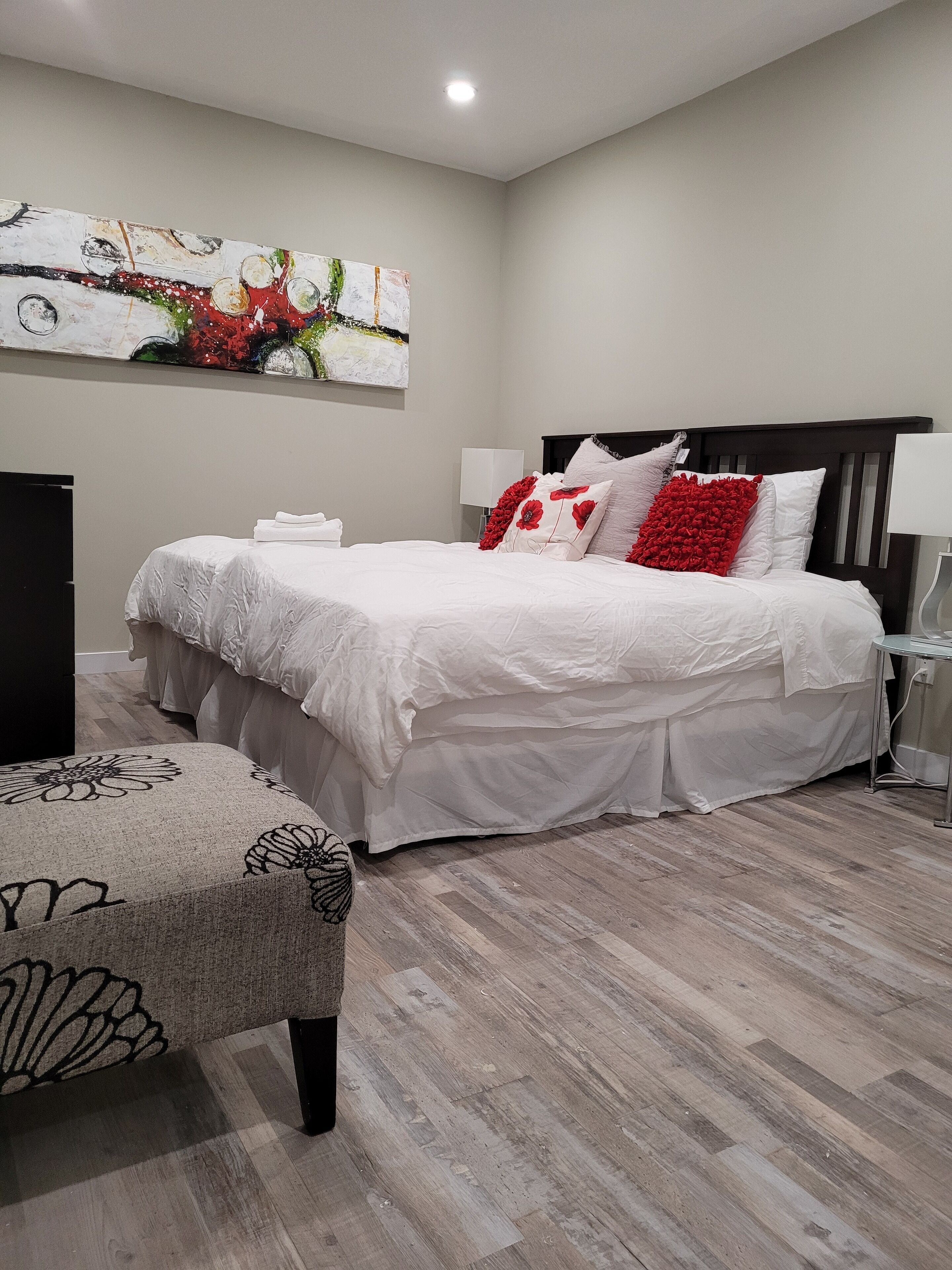 A modern bedroom with a large bed, a bedside table, a lamp, and a decorative wall piece.