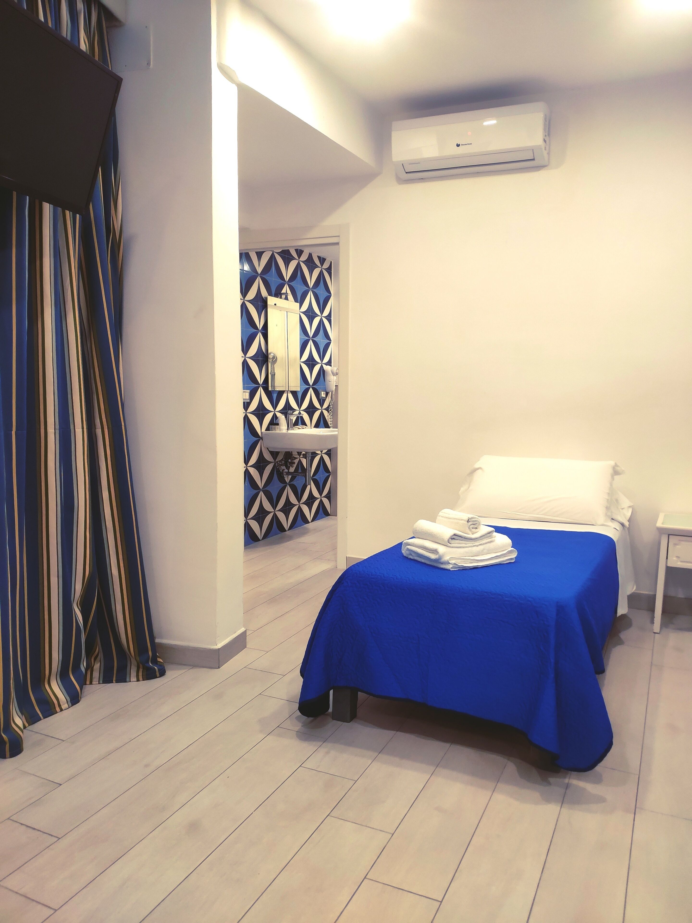 A hotel room with a bed, a nightstand, a mirror, and a bathroom with a towel rack.