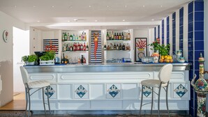 A bar area with two bar stools, shelves stocked with various bottles, and decorative items. - Hotel Oriente (Vico Equense)