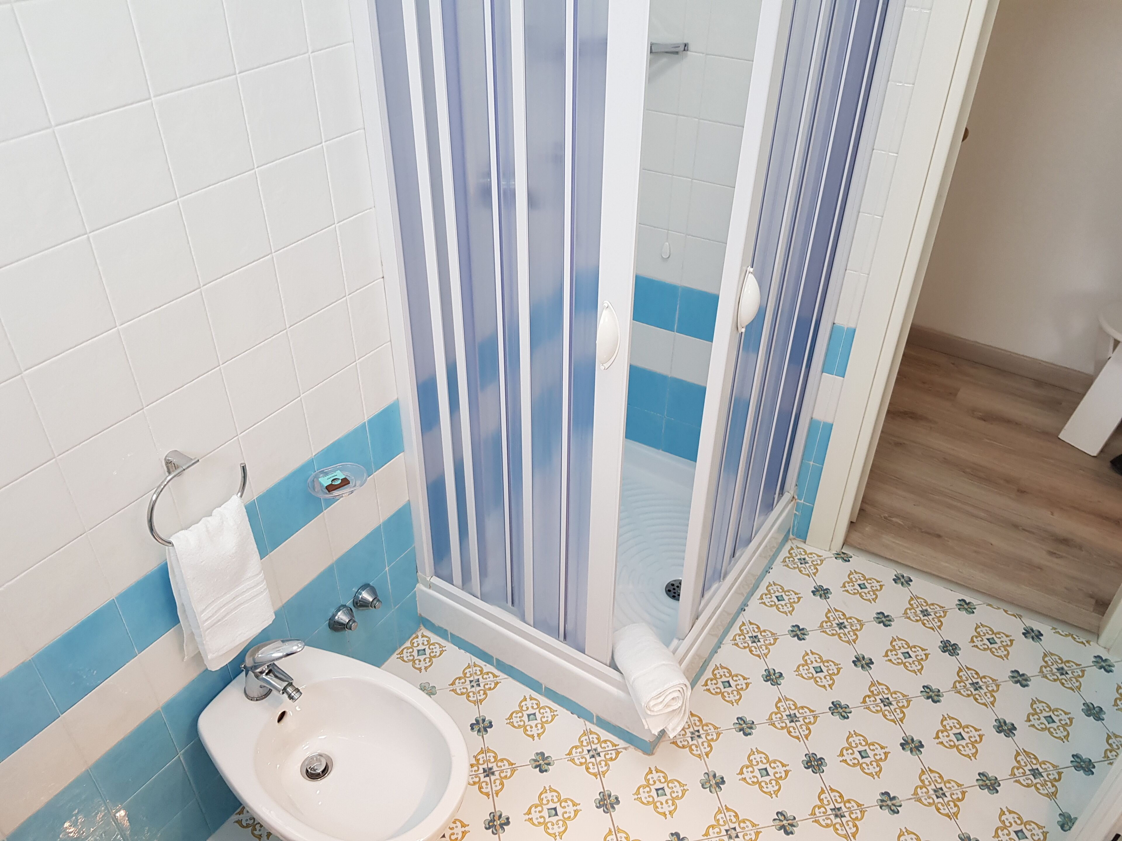 Ein Badezimmer mit einem weißen Waschbecken, blau-weißen Fliesen, einer Dusche mit Glastür und Fliesenboden mit Muster.