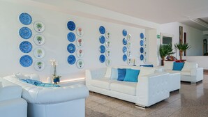 A modern living room with white sofas, blue cushions, and a wall decorated with blue and white plates with plants. - Hotel Oriente (Vico Equense)