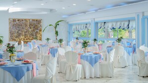 A banquet hall with round tables covered in blue and white tablecloths, white chairs, and potted plants. - Hotel Oriente (Vico Equense)