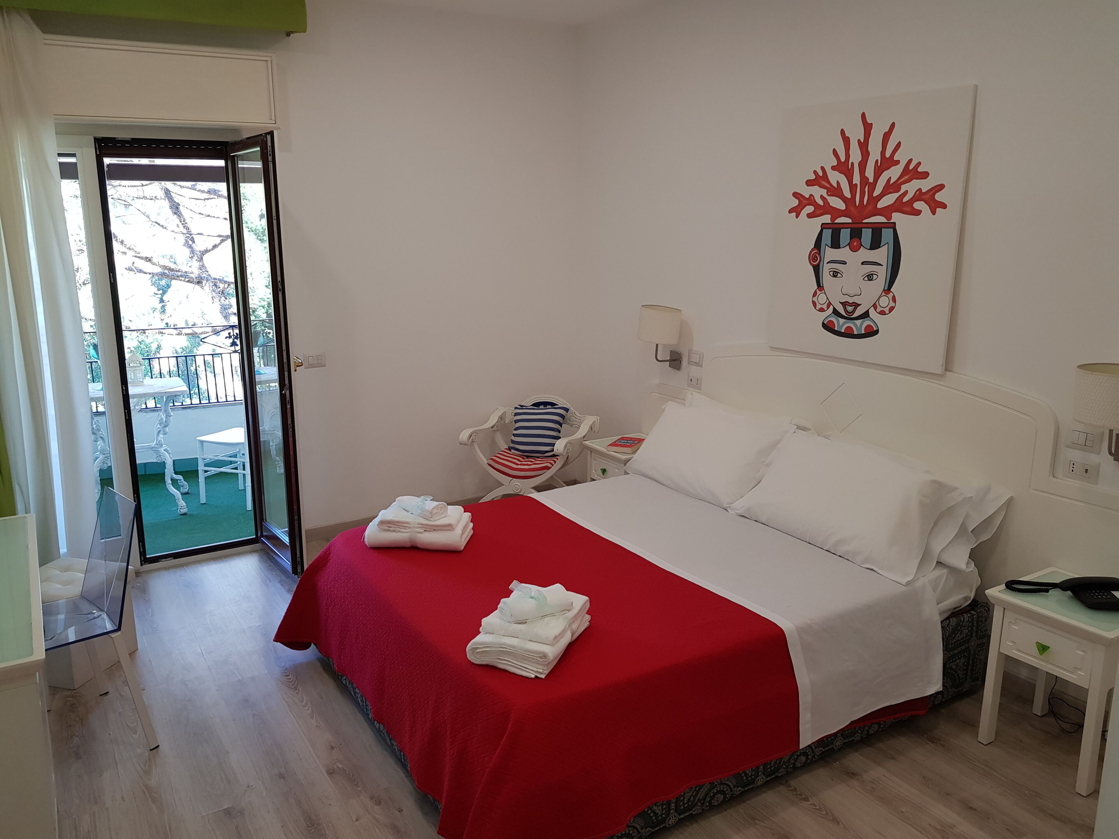 A hotel room with a bed, a chair, a table, and a balcony.