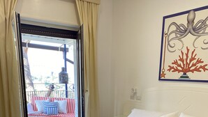 A hotel room with a bed, a red and blue bedspread, white pillows, and a painting of an octopus on the wall. - Hotel Oriente (Vico Equense)