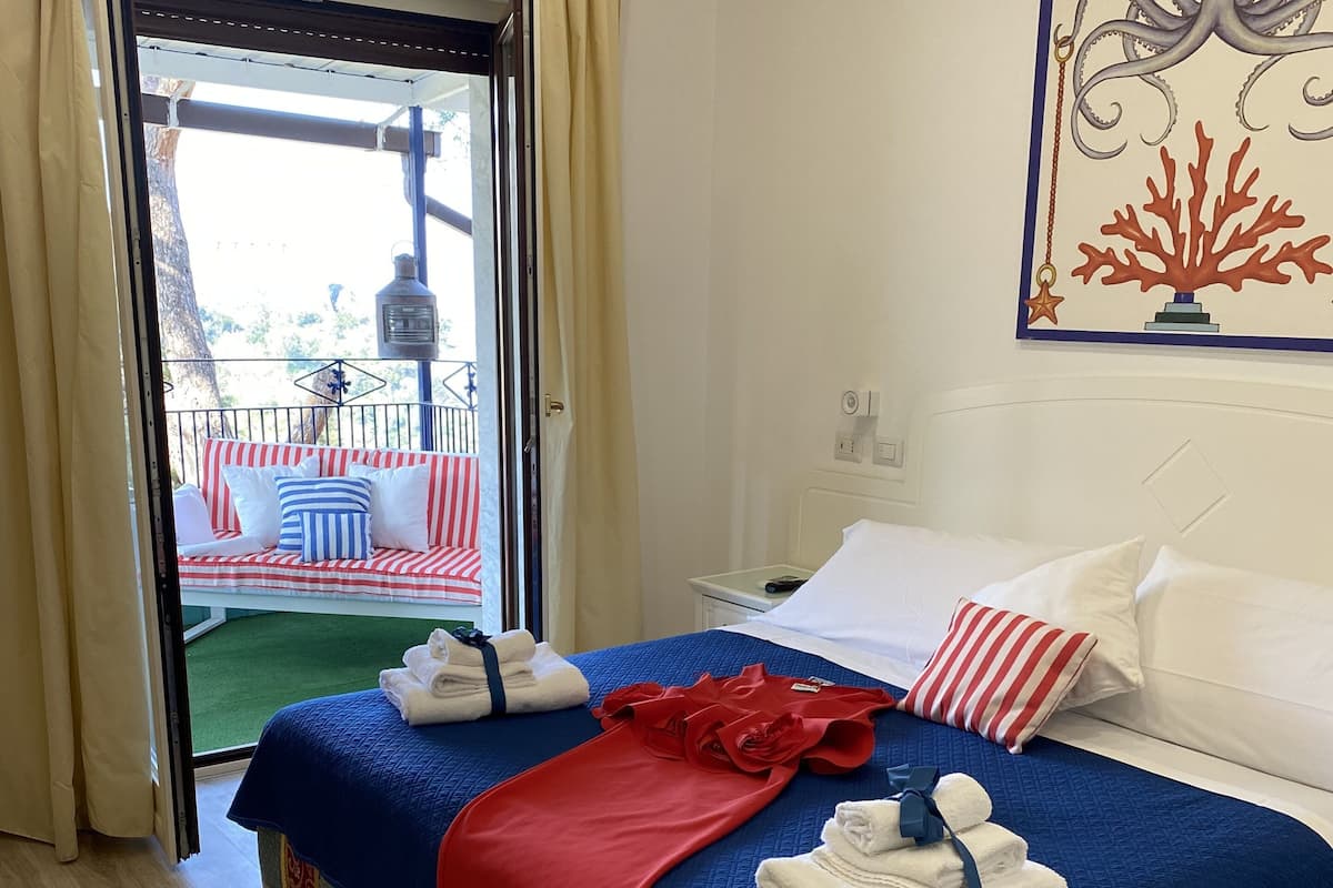 A hotel room with a bed, a red and blue bedspread, white pillows, and a painting of an octopus on the wall.