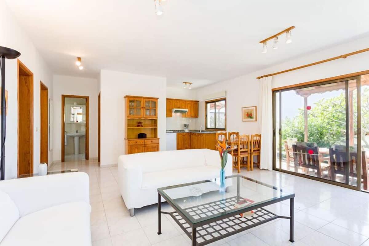 A spacious living area with a white sofa, a glass coffee table, and wooden cabinets.