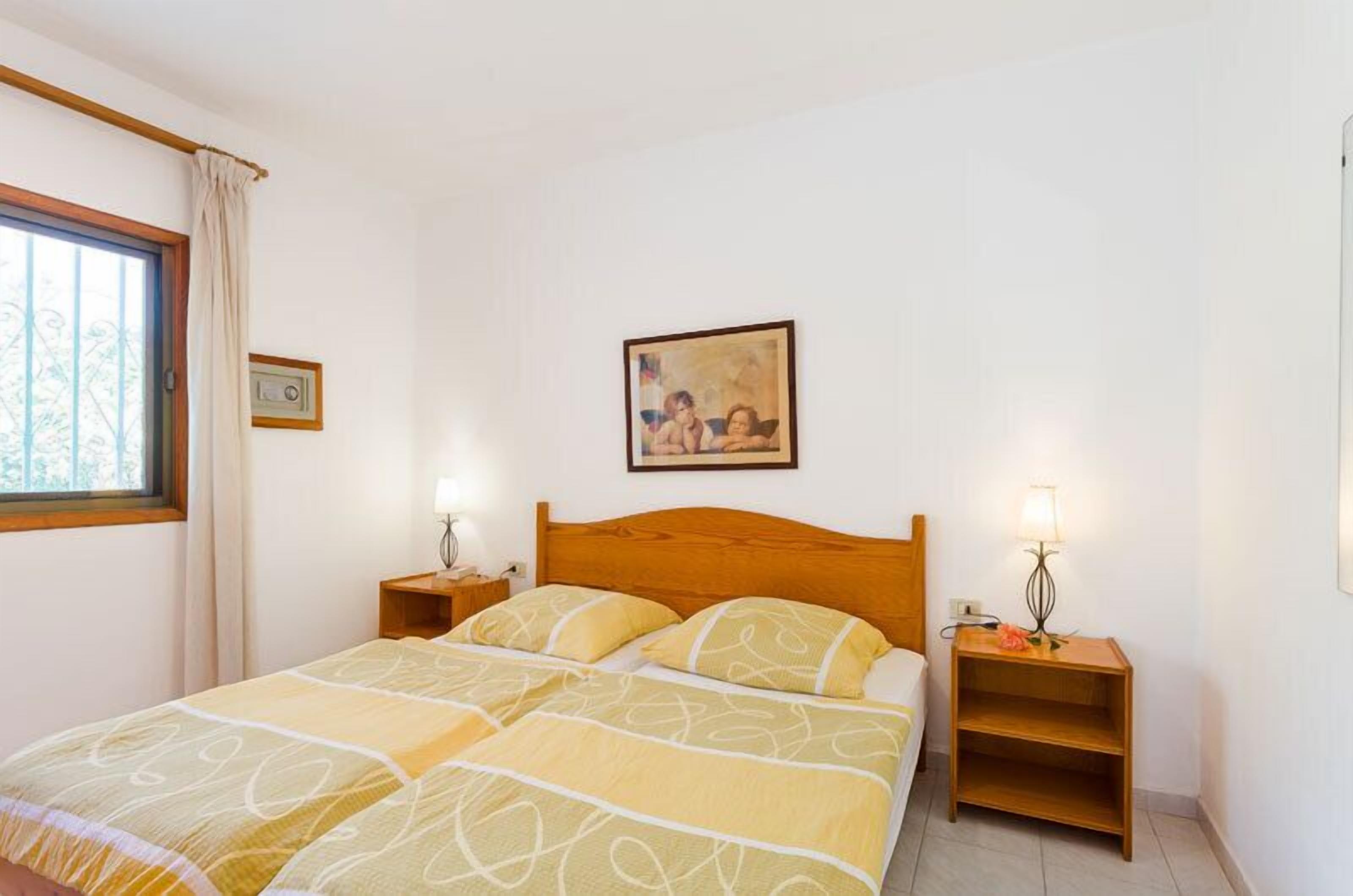 A bedroom with a bed, two bedside tables, a window with curtains, and a painting on the wall.