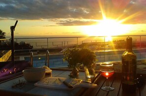 Vista al atardecer desde un balcón con piscina, una botella y una copa.