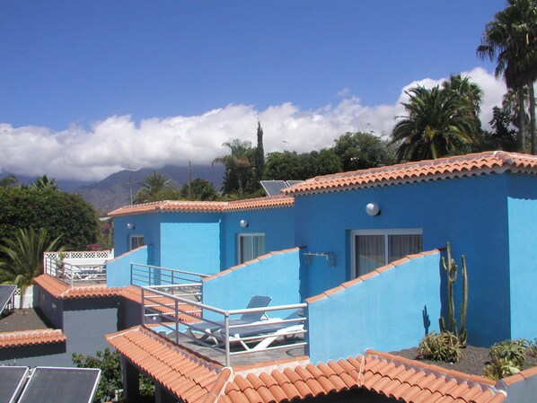 A blue building with a tiled roof, a balcony, and a view of mountains in the background. - Residencial Las Norias (Los Llanos de Aridane)