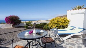 A round table with chairs and a sun lounger, set against a backdrop of a clear blue sky and a distant view of the sea. - Residencial Las Norias (Los Llanos de Aridane)