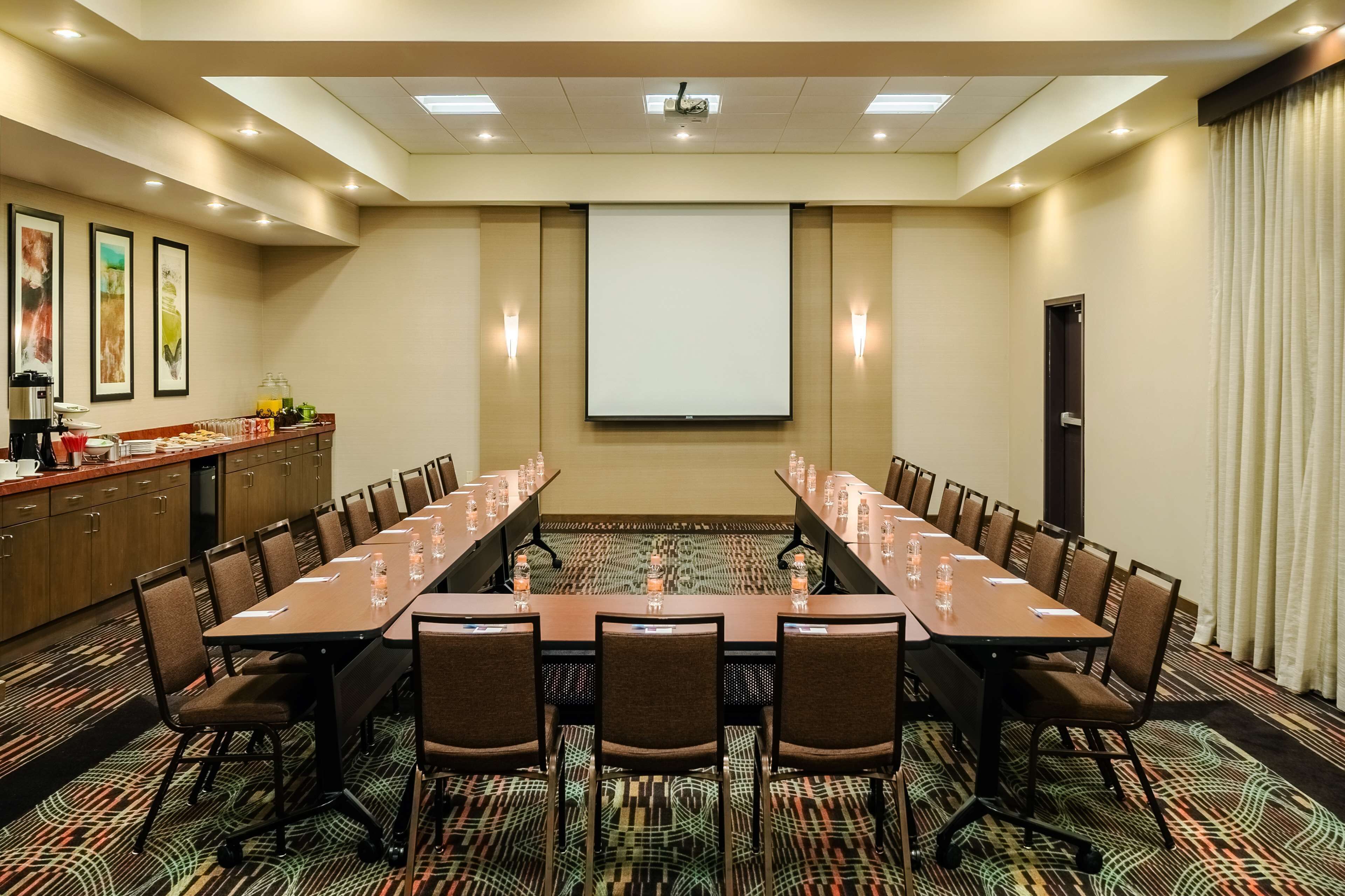 Una sala de conferències amb una taula llarga, cadires, una pantalla de projector i un espai per al cafè.