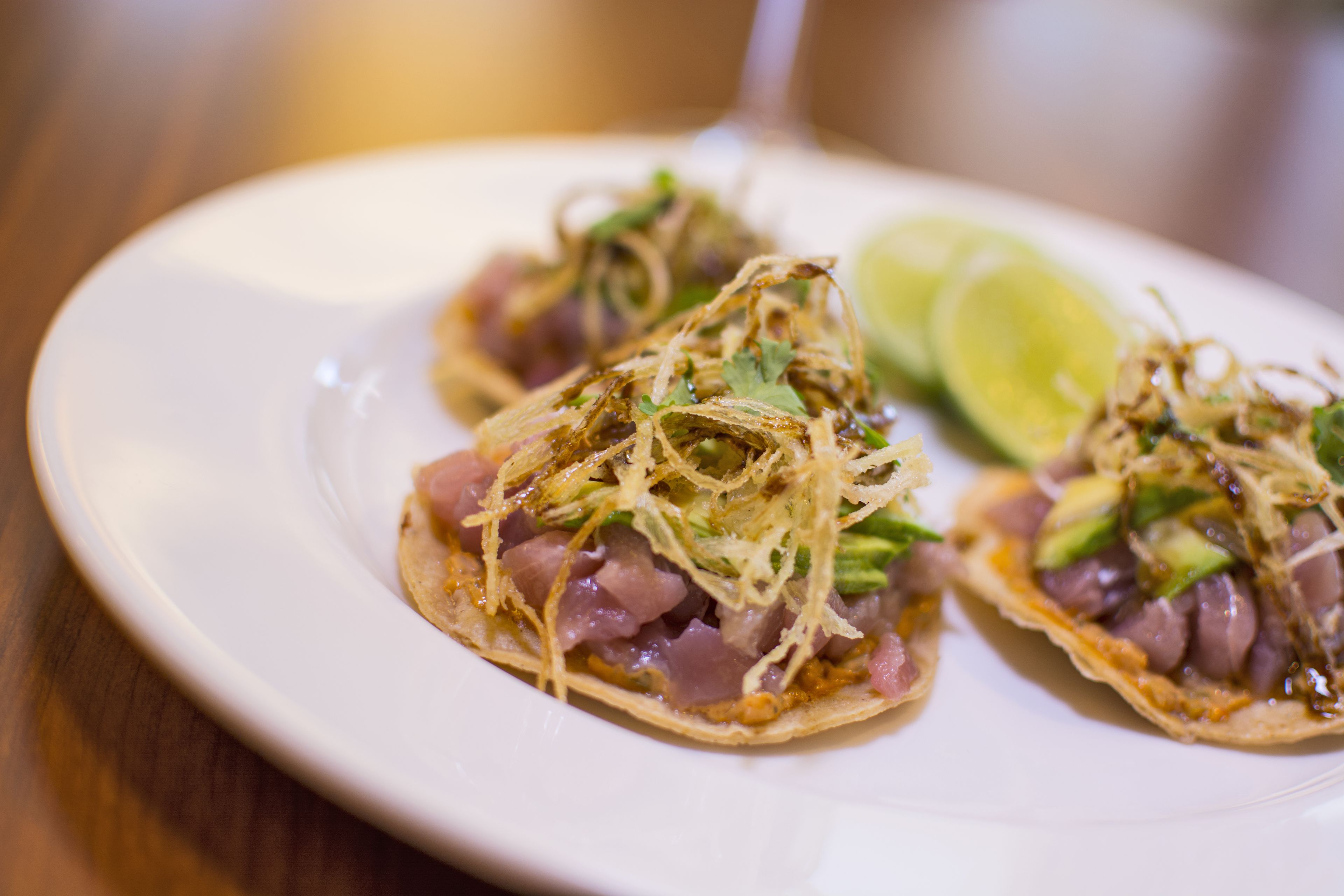 Een bord met drie taco's, elk belegd met stukjes kip, avocado en koriander, vergezeld van een partje limoen.