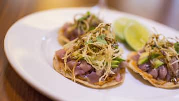 Een bord met drie taco's, elk belegd met stukjes kip, avocado en koriander, vergezeld van een partje limoen.