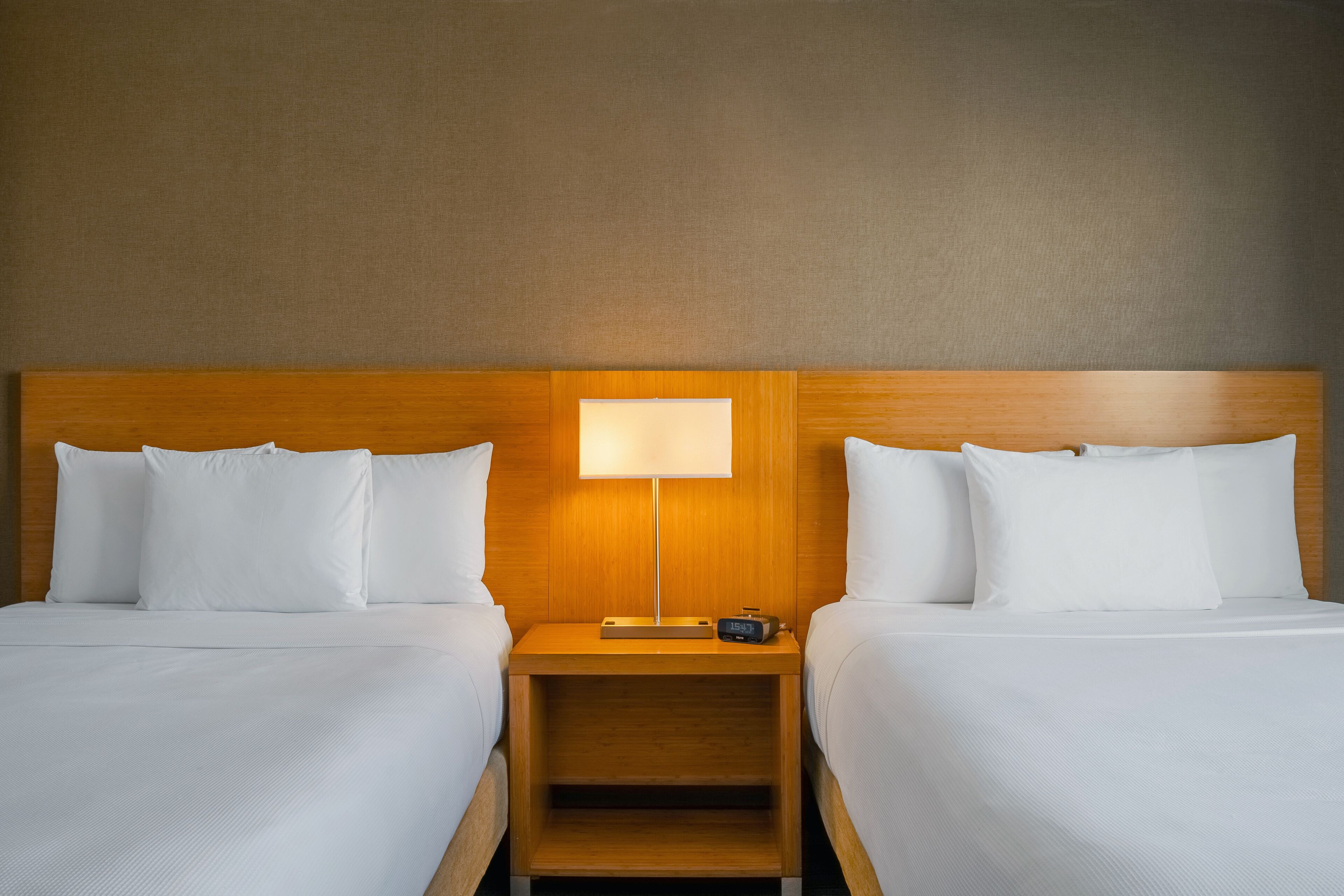 Een hotelkamer met twee bedden, een houten hoofdeinde, een nachtkastje met een lamp en een digitale klok.