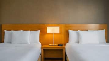 A hotel room with two beds, a wooden headboard, a nightstand with a lamp, and a digital clock.