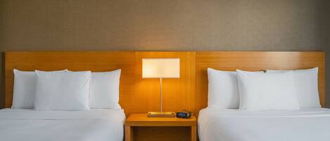 A hotel room with two beds, a wooden headboard, a nightstand with a lamp, and a digital clock.