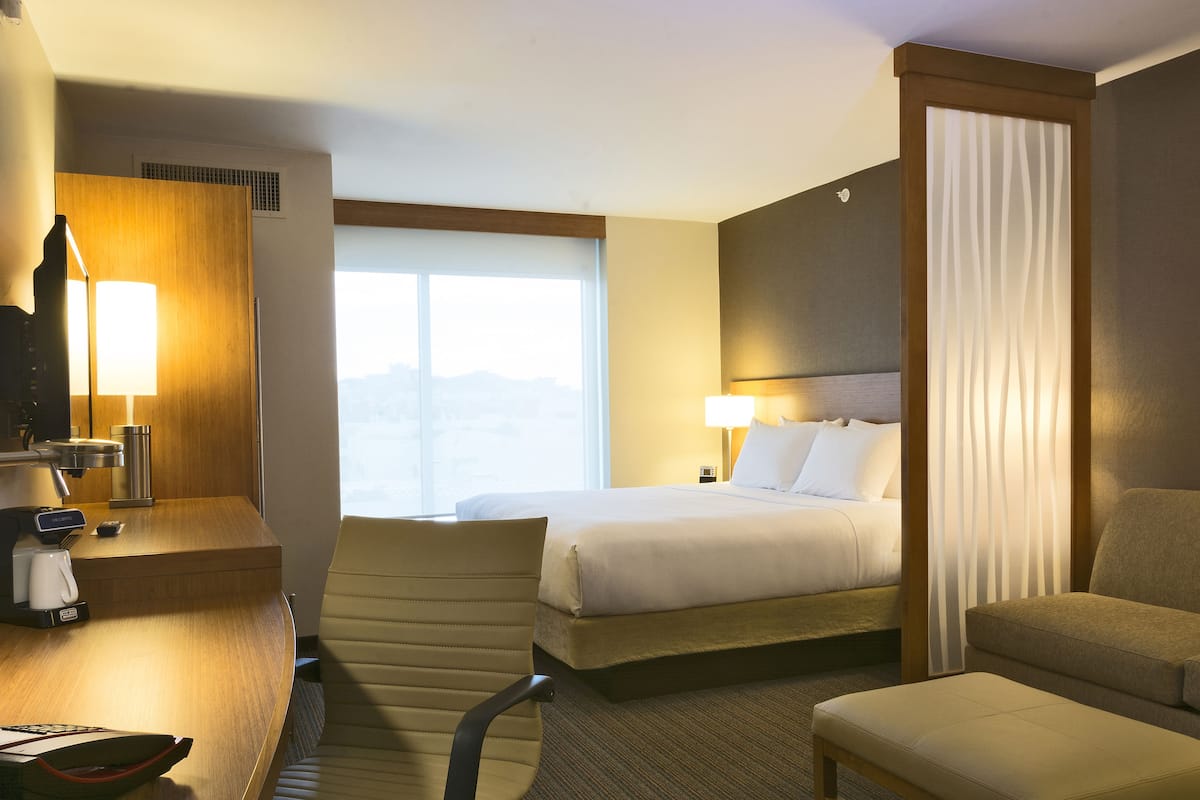 A hotel room with a bed, a desk with a lamp, a chair, and a view of the mountains through the window.