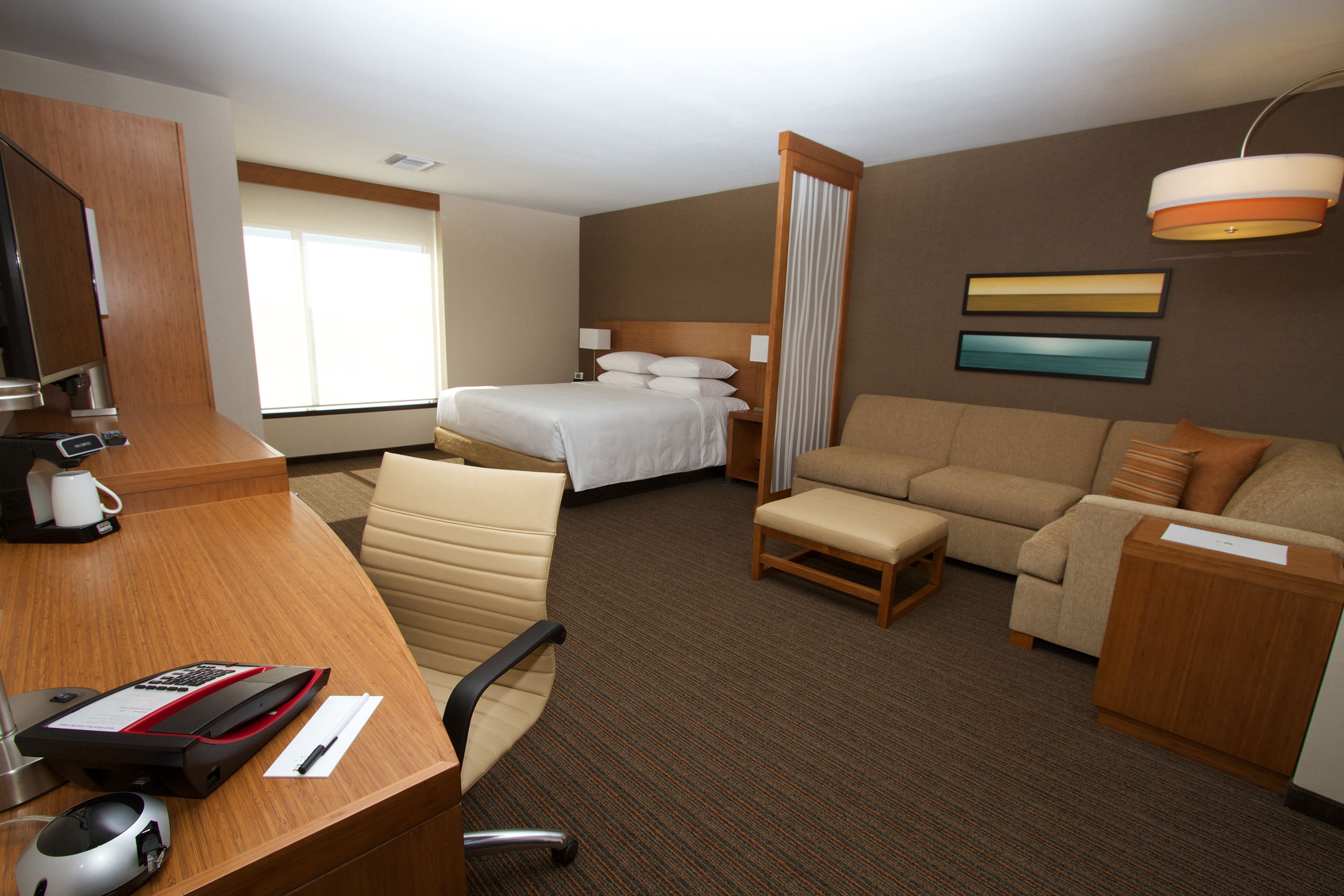 A hotel room with a bed, a sofa, a desk with a computer, a chair, and a coffee maker.